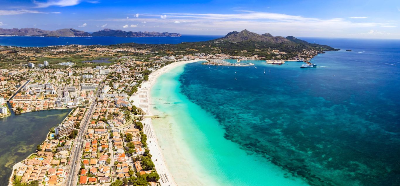 Panoramablick auf die Playa Muro und Alcúdia Luftaufnahme einer Küstenlandschaft mit Strand, blauem Wasser und grünen Hügeln.