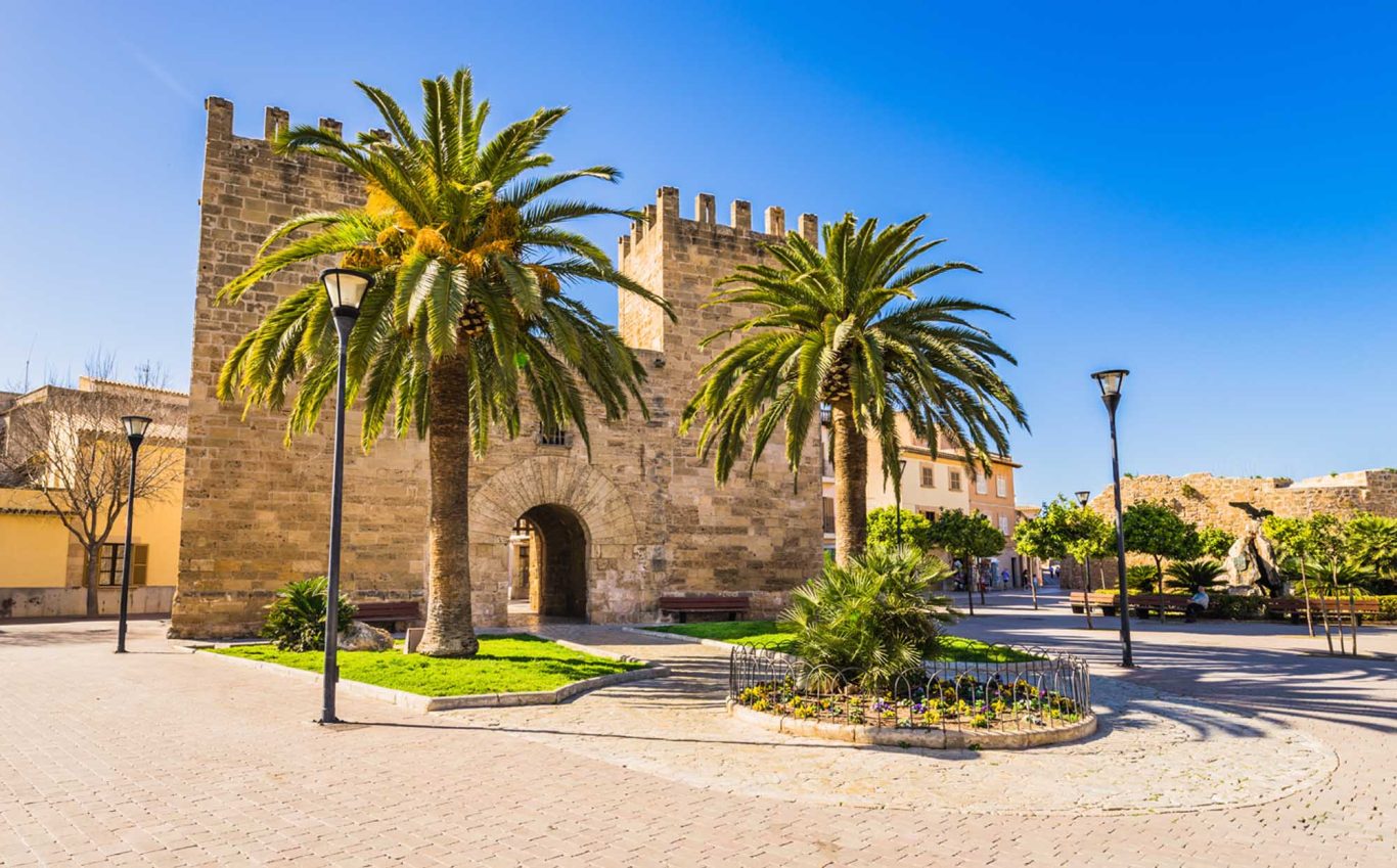 Historisches Stadttor Porta del Moll in der Altstadt von Alcúdia Historische Burg mit Palmen und blauem Himmel in einer sonnigen Umgebung.