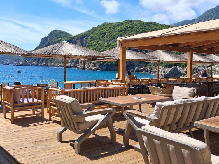 Strandbar auf Korfu an der Westküste Gemütliche Strandterrasse mit Holzstühlen und Sonnenschirmen, Blick auf das Meer.