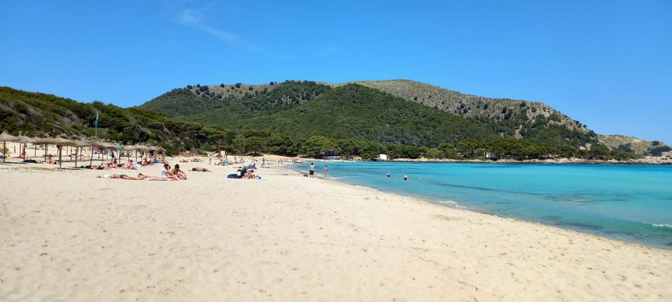 Sandstrand an der Cala Agulla Sandstrand mit Urlaubern und Berge