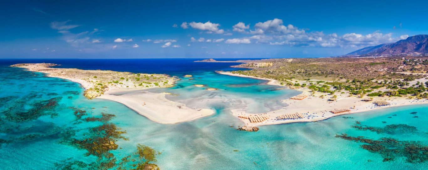 Elafonisi Strand mit klarem, blauem Wasser und rosa und weißem Sand, umgeben von Hügeln.
